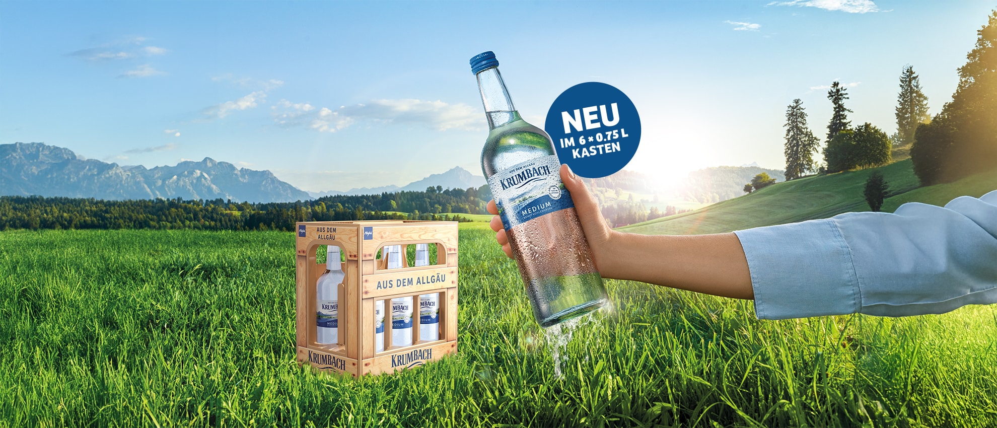 Hand hält Krumbach Mineralwasser (Medium) vor Allgäu-Kulisse, daneben 6er-Kasten. Text: „Einfach leicht – neu im 6 x 0,75 L Kasten“