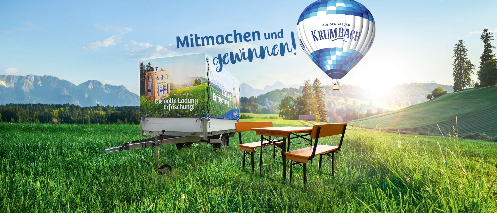 Allgäu-Landschaft mit grüner Wiese, Biertischgarnitur, Anhänger mit Krumbach-Werbung und Heißluftballon mit Schriftzug daneben „Mitmachen und gewinnen“.