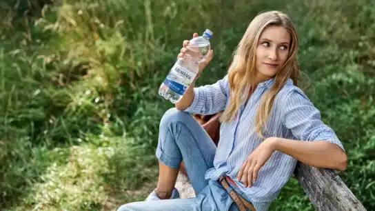 Frau auf Bank im Grünen mit einer Krumbach Mineralwasser-Flasche in der Hand