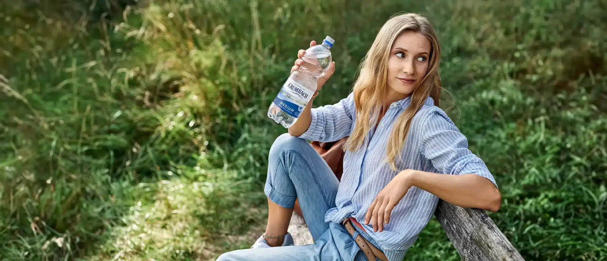 Frau auf Bank im Grünen mit einer Krumbach Mineralwasser-Flasche in der Hand