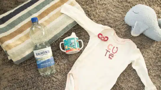 Krumbach Mineralwasser-Flasche neben Baby-Strampler und Trinkflasche