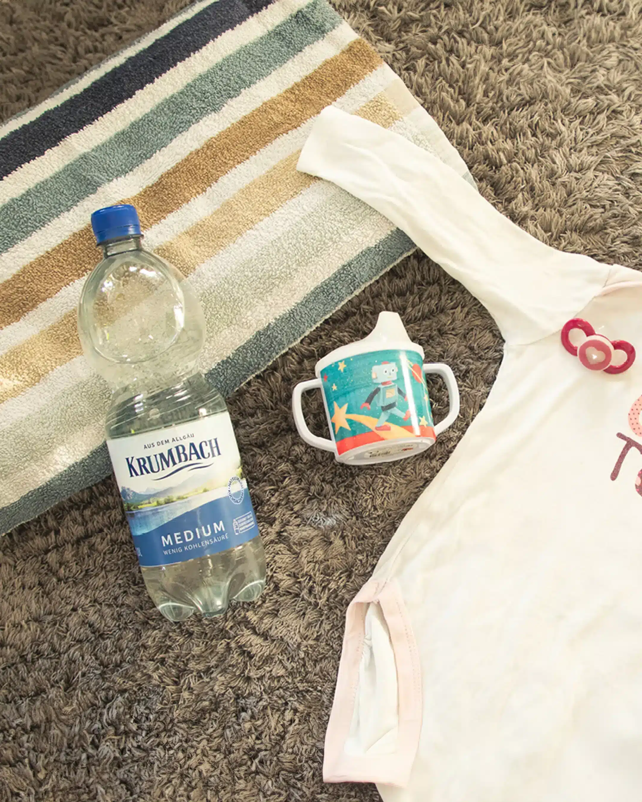 Krumbach Mineralwasser-Flasche neben Baby-Strampler und Trinkflasche