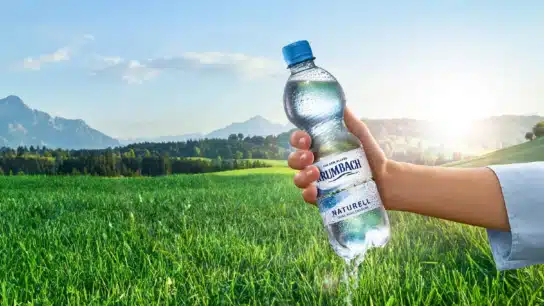 Frau mit Krumbach Naturell Flasche in der Hand vor idyllischer Berglandschaft
