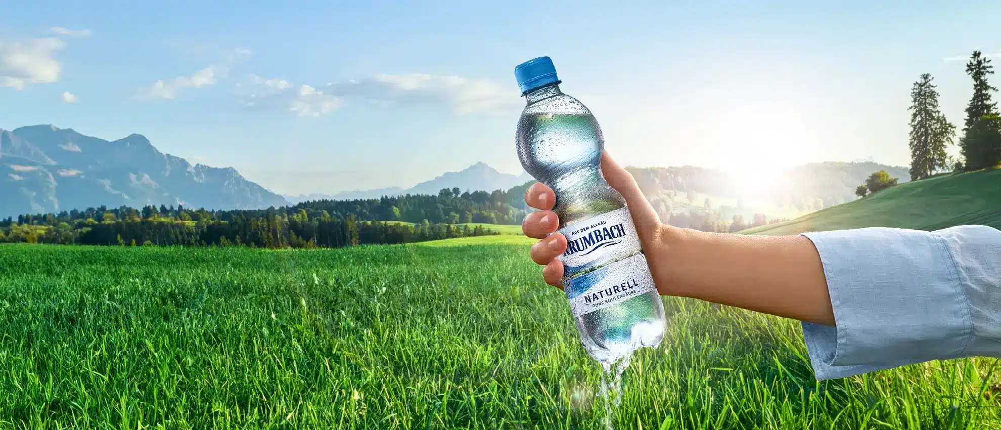 Frau mit Krumbach Naturell Flasche in der Hand vor idyllischer Berglandschaft
