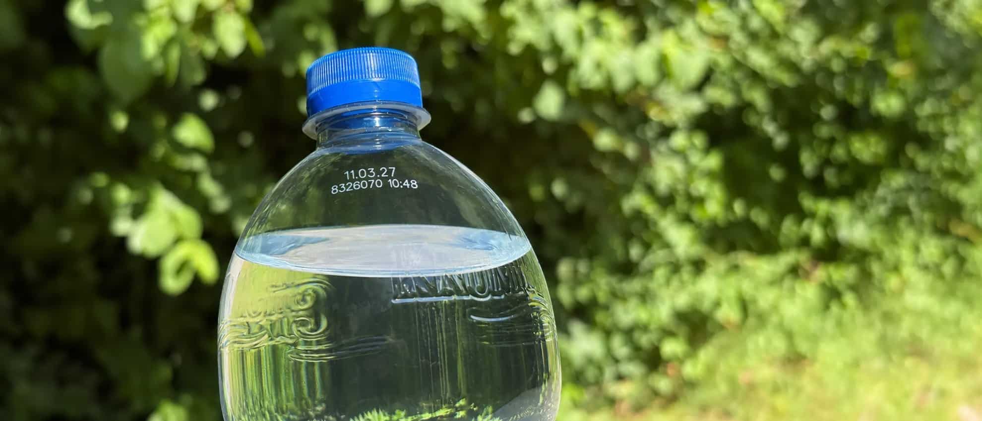 Krumbach PET-Flasche mit Mineralwasser und blauem Verschluss vor grüner Naturkulisse