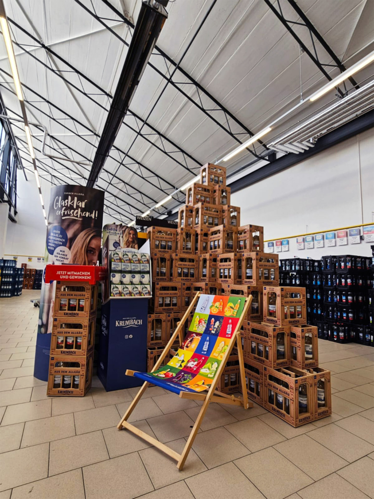 Krumbach Mineralwasser in Holz-Mehrwegkisten mit Aktionsdisplay und Liegestuhl in einem Getränkemarkt