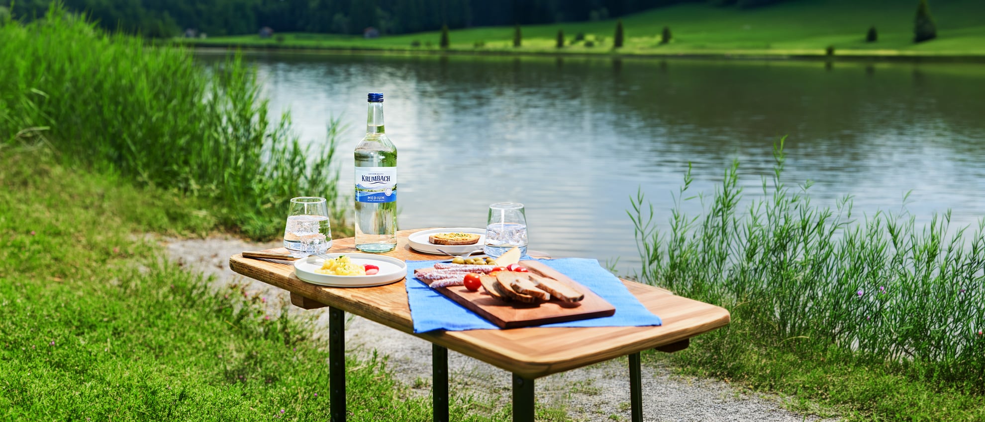 Picknicktisch mit Krumbach Medium Mineralwasser und Brotzeit am See in der Allgäuer Natur