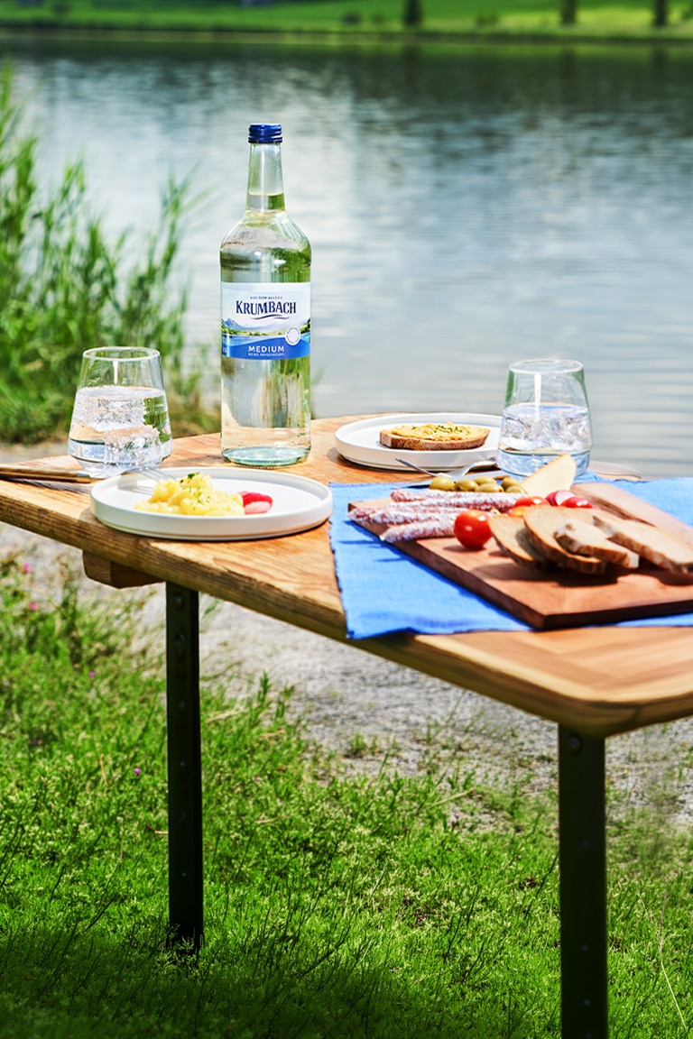 Picknicktisch mit Krumbach Medium Mineralwasser und Brotzeit am See in der Allgäuer Natur